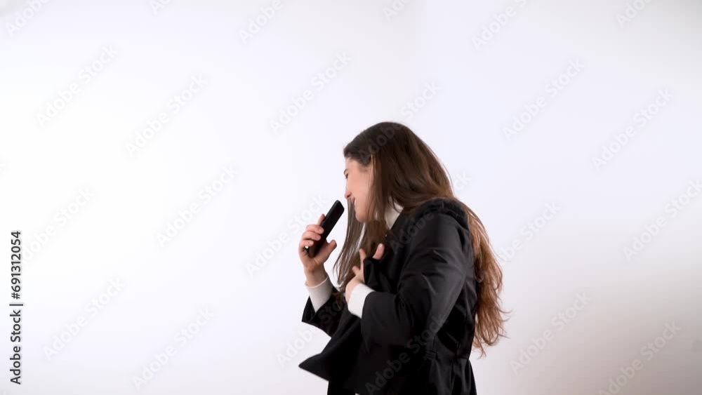 Charming young female in elegant suit smiling and singing song into smartphone while outstretching hand up against white background Charming young female in elegant suit smiling and singing song into smartphone while outstretching hand up against white background