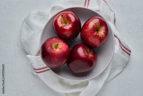 Red apples in a white bowl placed on a red white cloth on a white background.