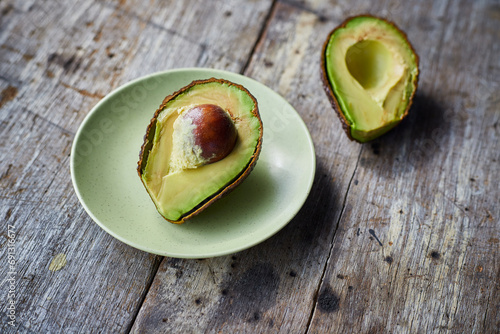 Avocado cut in half Placed on a light green plate on a wooden background.
