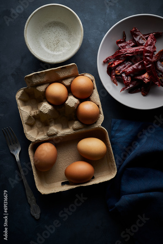 Clusters of eggs are placed on the package. with dried red chilies in a bowl and Fork on a blue-gray background.