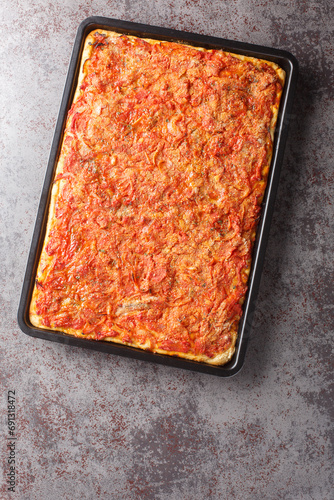 Delicious Italian Sfincione focacia with onions, tomatoes, cheese, anchovies and breadcrumbs closeup on a baking sheet on the table. Vertical top view from above photo