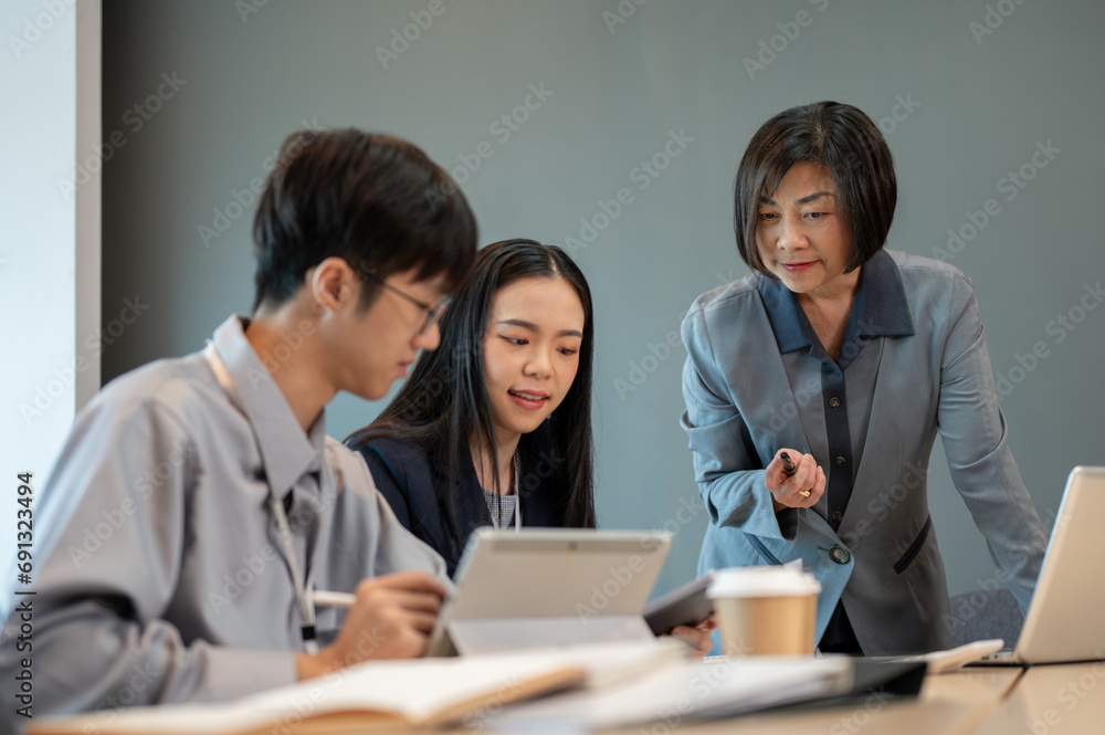 A professional senior Asian female boss is coaching to her employees in the meeting. A professional senior Asian female boss is coaching to her employees in the meeting.