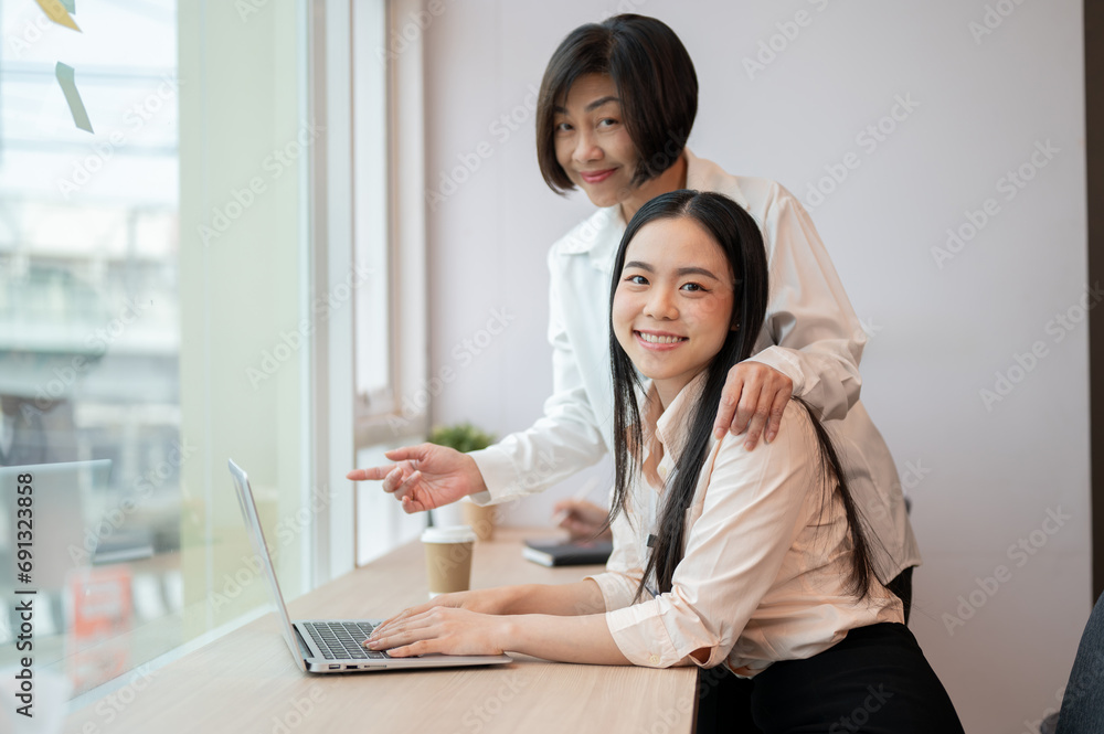 A kind senior Asian female boss is helping and coaching a new project for a young colleague.