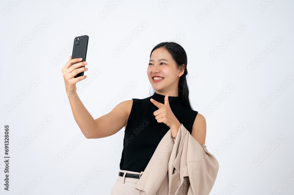 A cheerful Asian businesswoman is pointing her finger at her smartphone screen while using it. A cheerful Asian businesswoman is pointing her finger at her smartphone screen while using it.