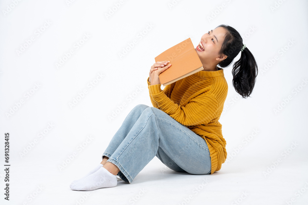 Young pretty Asian woman in casual clothes sits on an isolated studio white background with a book.