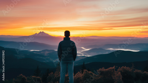 A person standing on a mountain top, looking out at a beautiful sunset