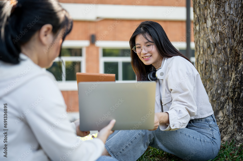 A positive young Asian female college student is doing home work with her friend in a campus park. A positive young Asian female college student is doing home work with her friend in a campus park.
