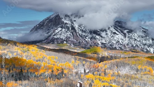 Kebler Pass aerial cinematic drone Crested Butte Gunnison Colorado seasons collide early fall aspen tree red yellow orange forest winter first snow powder Rocky Mountain peak dirt road backward motion photo