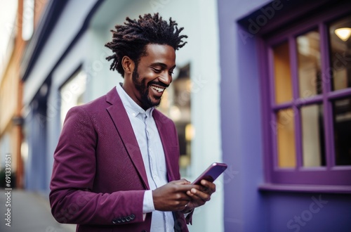 a smiling man looking at his phone while standing on a purple street wall