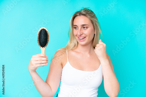 Young caucasian woman with hair comb isolated on blue background celebrating a victory