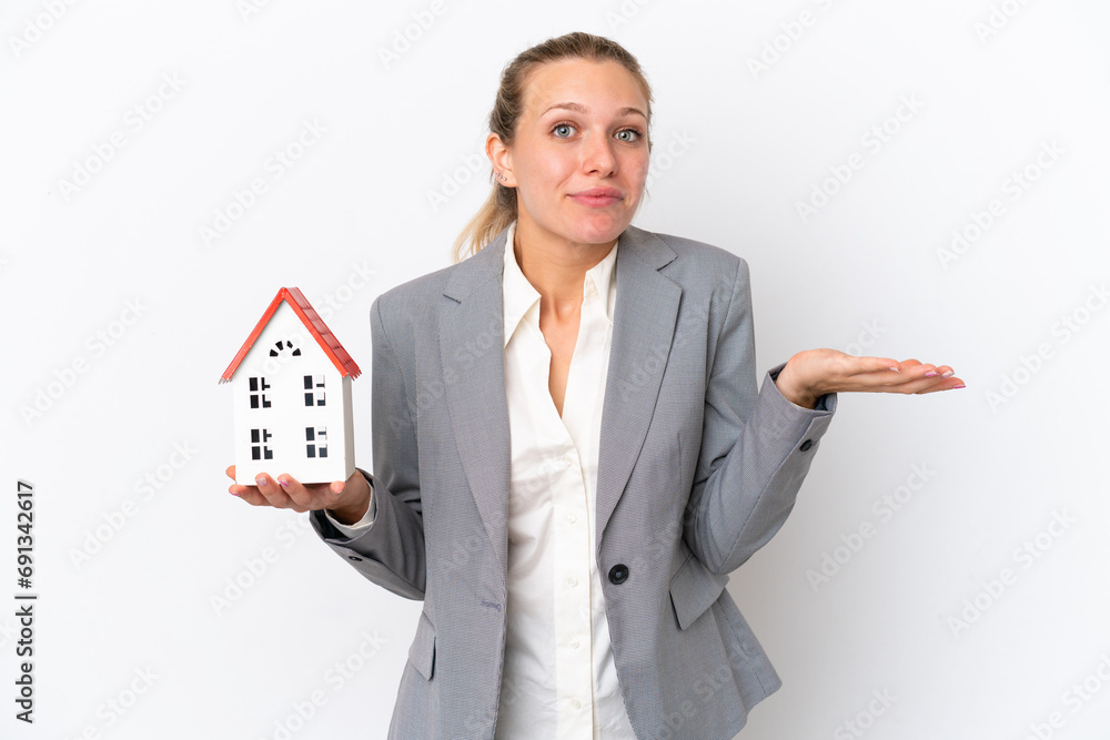 Real estate agent woman holding a toy house isolated on white background having doubts while raising hands Real estate agent woman holding a toy house isolated on white background having doubts while raising hands