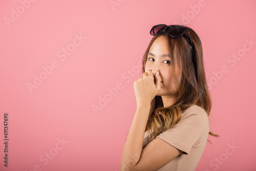 Asian beautiful young woman unhappy what a smell disgust expression squeezing nose with fingers. Female have something stinks bad smell situation, studio shot isolated on pink background, Healthcare photo