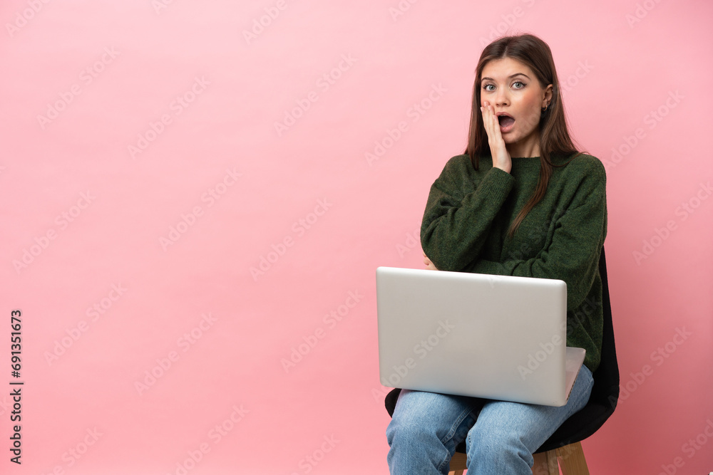 Young caucasian woman sitting on a chair with her laptop isolated on pink background surprised and shocked while looking right Young caucasian woman sitting on a chair with her laptop isolated on pink background surprised and shocked while looking right