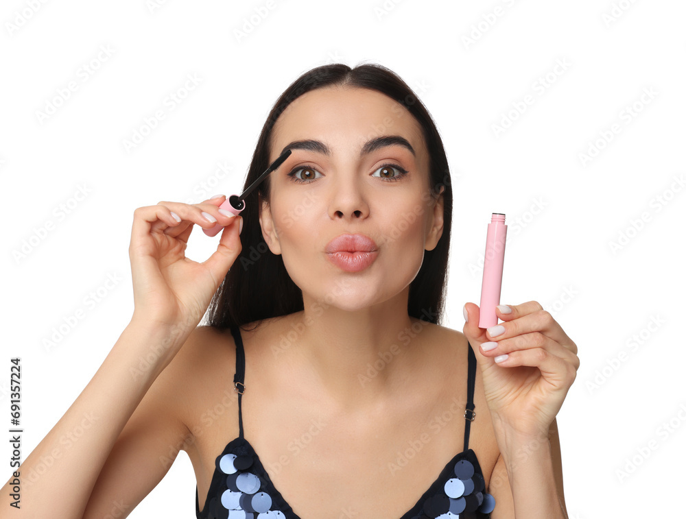 Beautiful young woman sending air kiss while applying mascara on white background