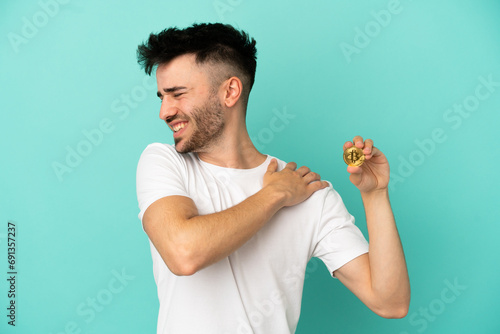 Young man holding a Bitcoin isolated on blue background suffering from pain in shoulder for having made an effort photo