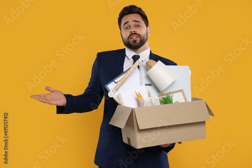 Confused unemployed man with box of personal office belongings on orange background © New Africa