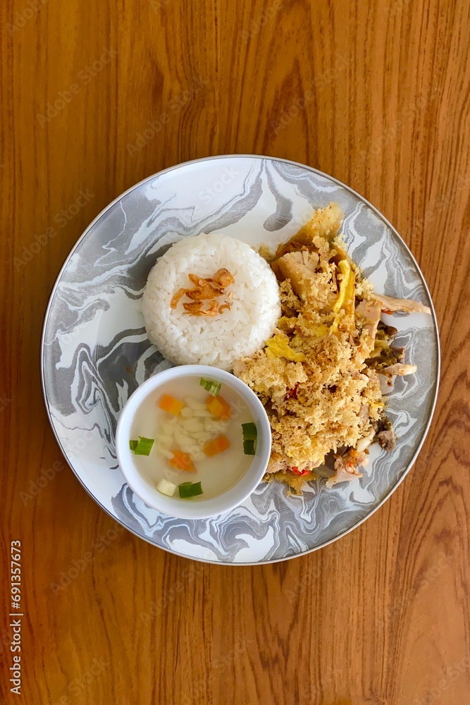 Indonesian food Ayam Geprek nasi served with traditional soup, rice, fried onion, and kremes put on wooden texture table