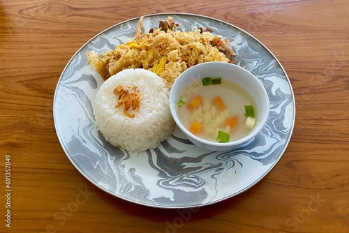 Indonesian food Ayam Geprek nasi served with traditional soup, rice, fried onion, and kremes put on wooden texture table