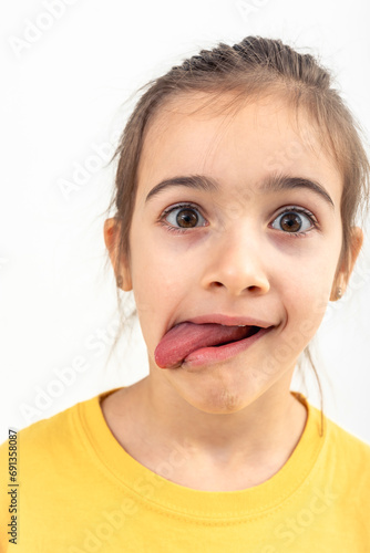 A little girl grimaces with her tongue hanging out on a white background. © puhimec