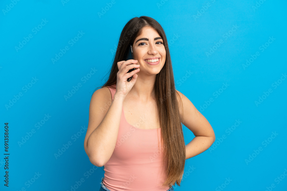 Young caucasian woman isolated on blue background keeping a conversation with the mobile phone Young caucasian woman isolated on blue background keeping a conversation with the mobile phone
