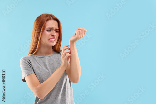 Suffering from allergy. Young woman scratching her arm on light blue background, space for text photo