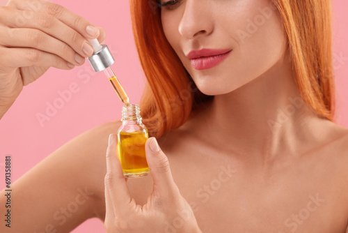 Beautiful young woman with bottle of cosmetic serum on pink background, closeup