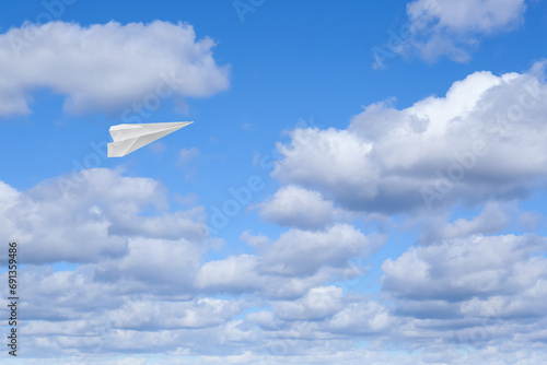 White paper plane flying in blue sky with clouds