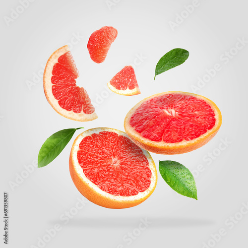 Pieces of grapefruit and green leaves falling on light gray background photo