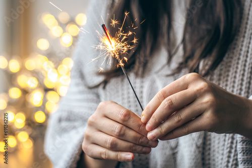 Woman with gray sweater holding a sparkling sparkler in her hands, close up.