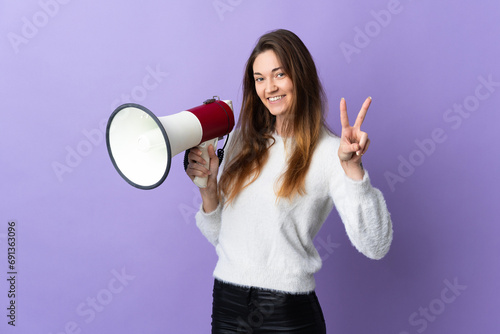 Young Ireland woman isolated on purple background holding a megaphone and smiling and showing victory sign