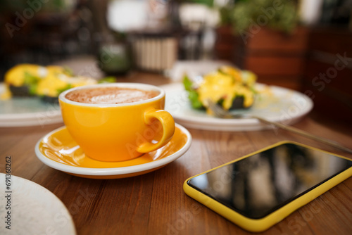 Yellow coffee cup with smart phone on table at cafe photo