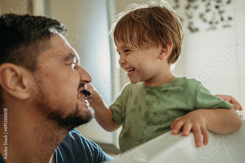 Playful boy brushing father's teeth in bathroom at home photo