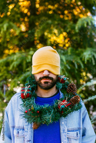 Man covering eyes with knit hat and wearing Christmas wreath around neck photo