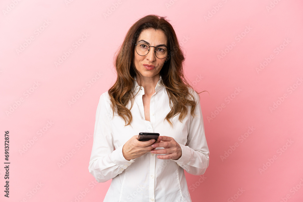 Middle aged caucasian woman isolated on pink background sending a message with the mobile Middle aged caucasian woman isolated on pink background sending a message with the mobile