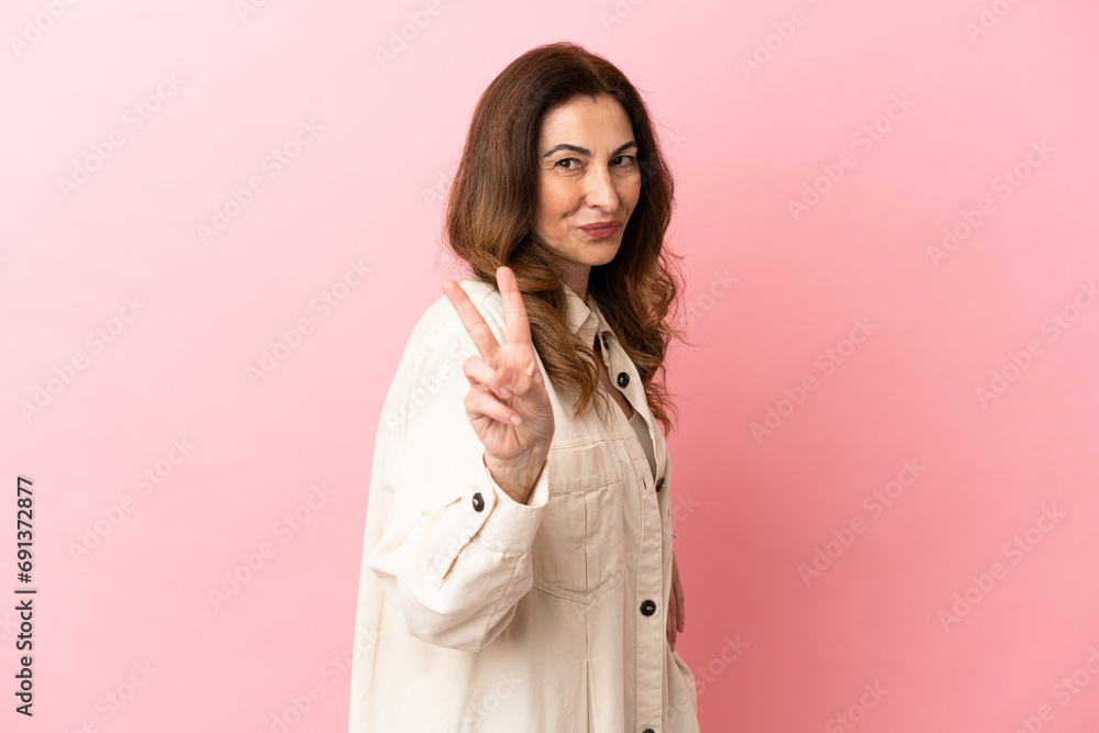 Middle aged caucasian woman isolated on pink background smiling and showing victory sign Middle aged caucasian woman isolated on pink background smiling and showing victory sign