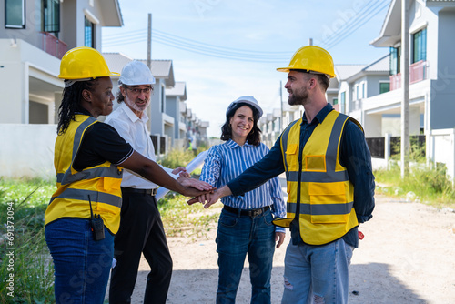 Multiracial engineers man with hands shaking hands with african american architect while standing near house building with blueprints in a housing project Team and construction concept
