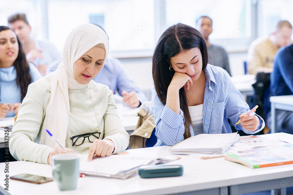 Multi-ethnic students with books on desk studying together in classroom Multi-ethnic students with books on desk studying together in classroom
