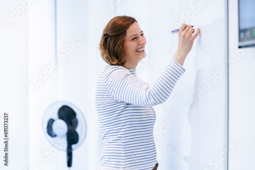 Happy teacher writing on whiteboard and teaching in classroom photo