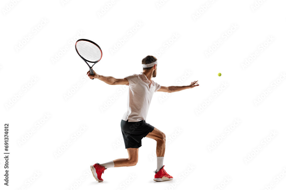 Concentered young man, tennis payer in motion during game, training, hitting ball with racket isolated over white background. Concept of sport, hobby, active and healthy lifestyle, competition
