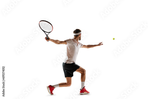 Concentered young man, tennis payer in motion during game, training, hitting ball with racket isolated over white background. Concept of sport, hobby, active and healthy lifestyle, competition © master1305