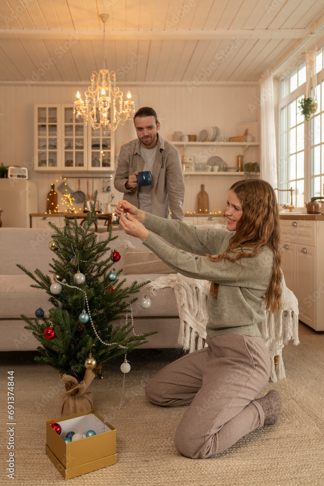 Smiling woman decorating Christmas tree with man standing at home Smiling woman decorating Christmas tree with man standing at home