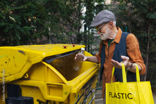 Senior man throwing plastic waste, bottles into recycling container in front apartment. Elderly man sorting the waste according to material into colored bins. photo