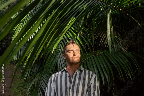 Smiling young man with sunlight over face near palm leaves photo
