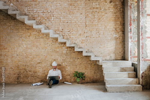 Architect using laptop and sitting under staircase at construction site photo