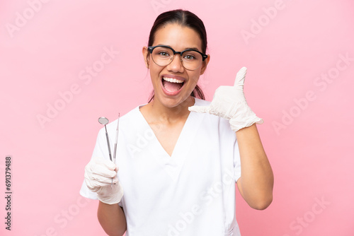 Dentist Colombian woman isolated on pink background making phone gesture. Call me back sign photo