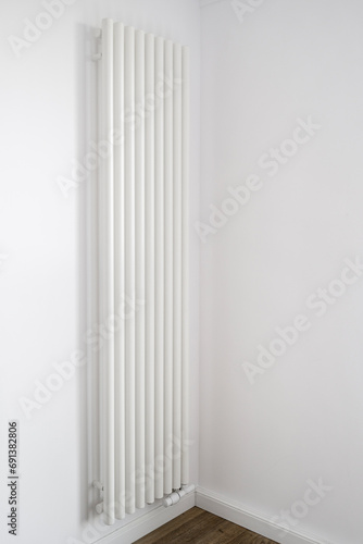 Vertical radiator install on white wall in empty room with minimalist interior