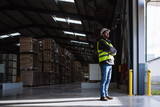 Portrait of warehouse worker taking break from work, standing and looking outdoors. Worker in reflective clothes, with copy space.
