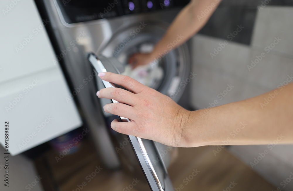 Woman hand fills drum of washing machine. Household chores and turning on washing machine concept