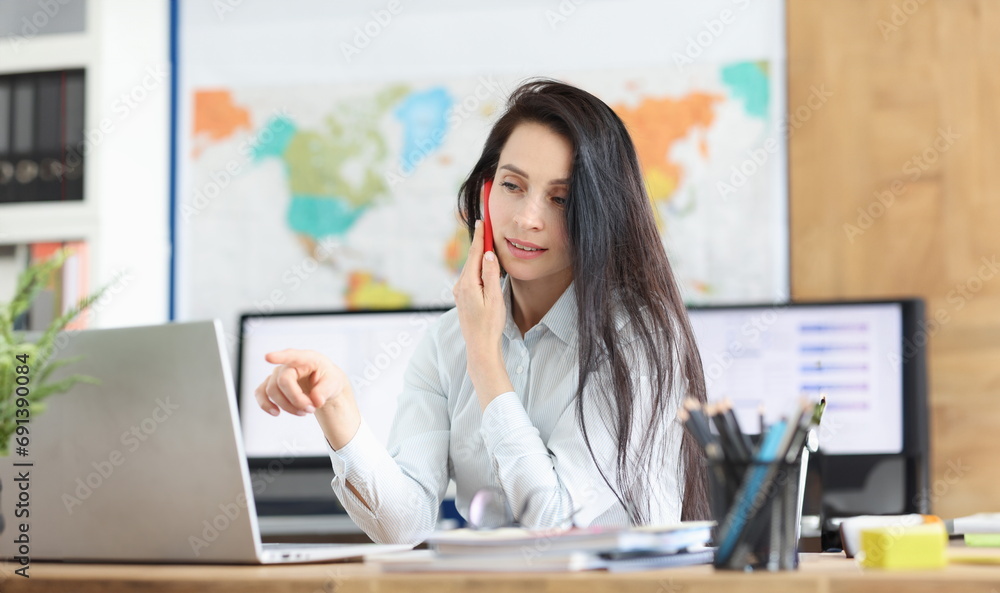 Business consultant positively talking on mobile phone working on laptop in office. Secretary enjoying work process and talking on smartphone concept Business consultant positively talking on mobile phone working on laptop in office. Secretary enjoying work process and talking on smartphone concept