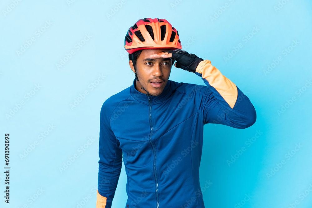 Young cyclist man with braids over isolated background looking far away with hand to look something Young cyclist man with braids over isolated background looking far away with hand to look something